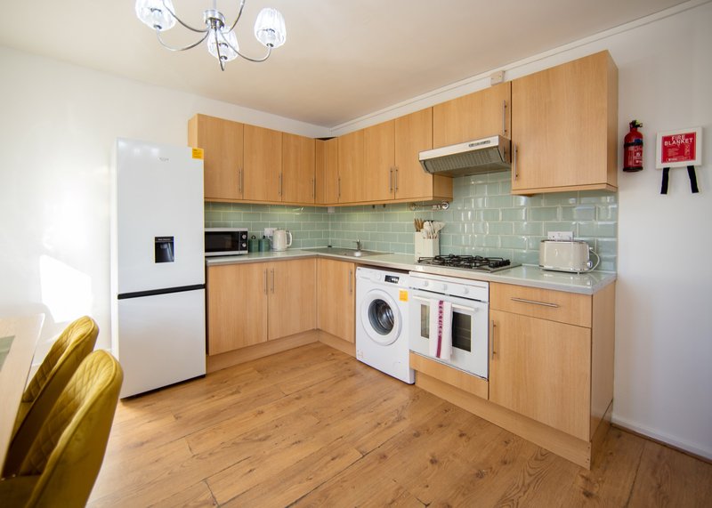 Modern kitchen with wooden cabinets, white appliances, green tile backsplash and wooden flooring