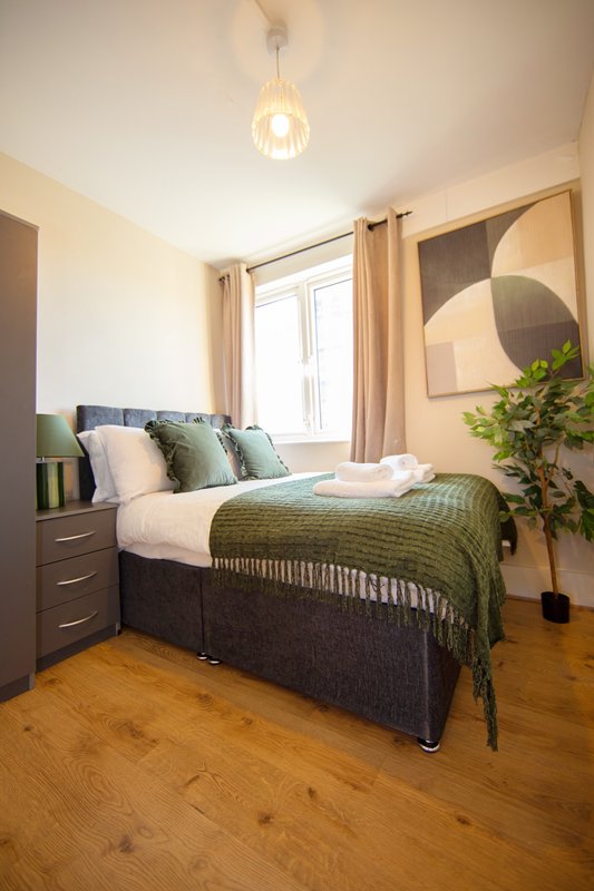 Modern bedroom with double bed, green bedding, wooden flooring and pendant light fixture