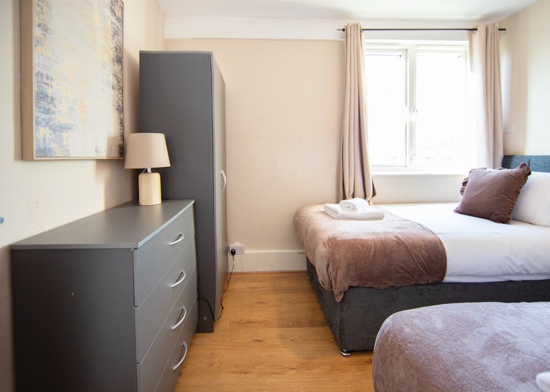 Bedroom with two beds, dark dresser, lamp, framed artwork and window with curtains
