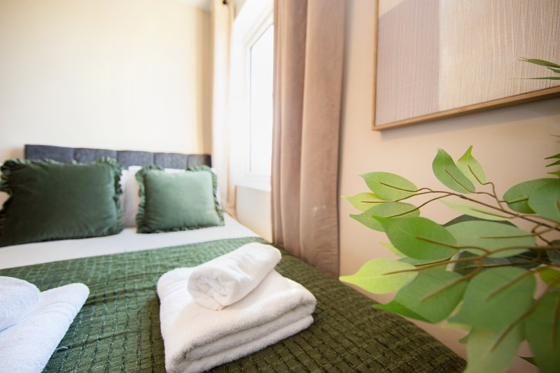 Bedroom with double bed, green bedding, cushions, fresh towels and potted plant