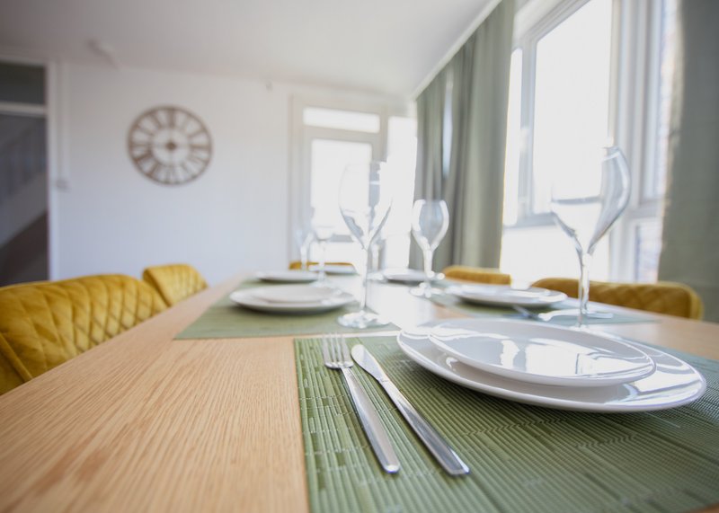 Modern dining room with wooden table, yellow chairs, place settings and large windows