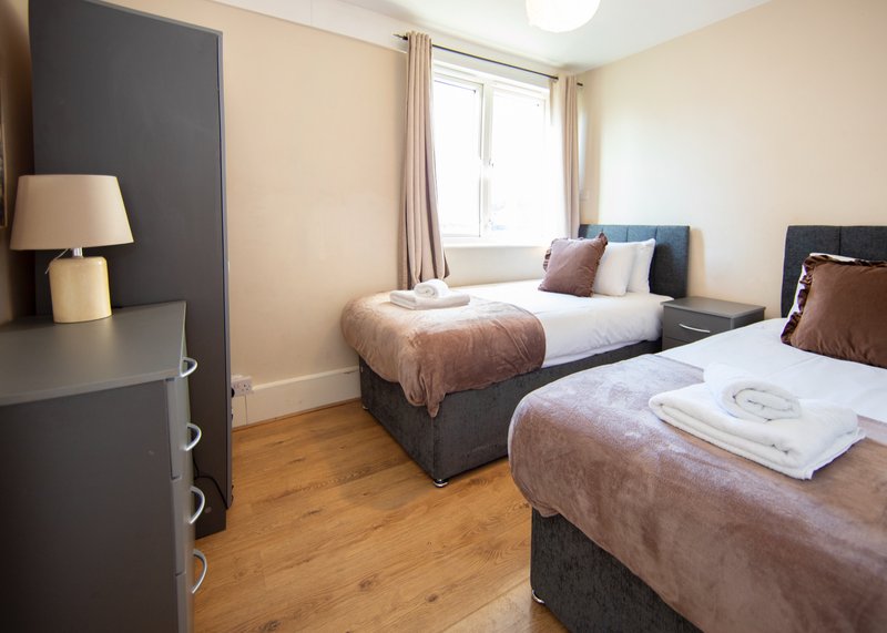 Spacious twin bedroom with two beds, wooden floor, lamp and window with curtains