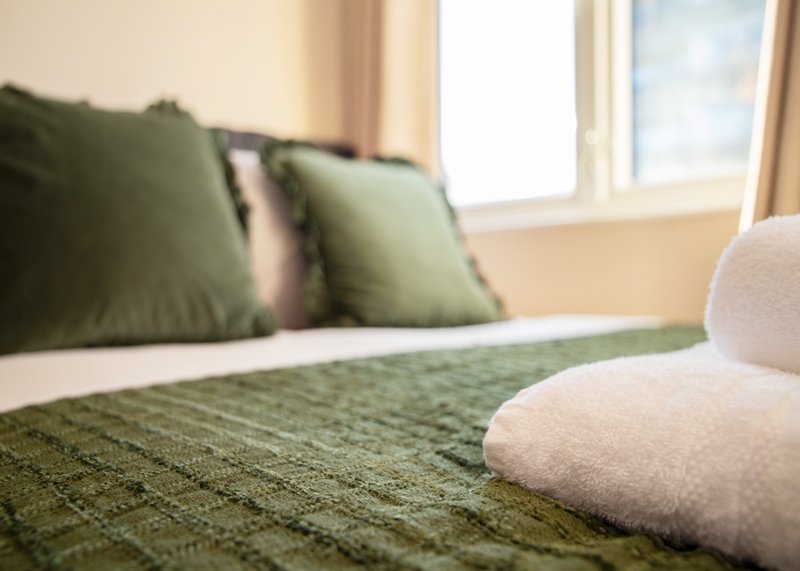 Bedroom with green cushions, white pillow, textured bedspread and bright window