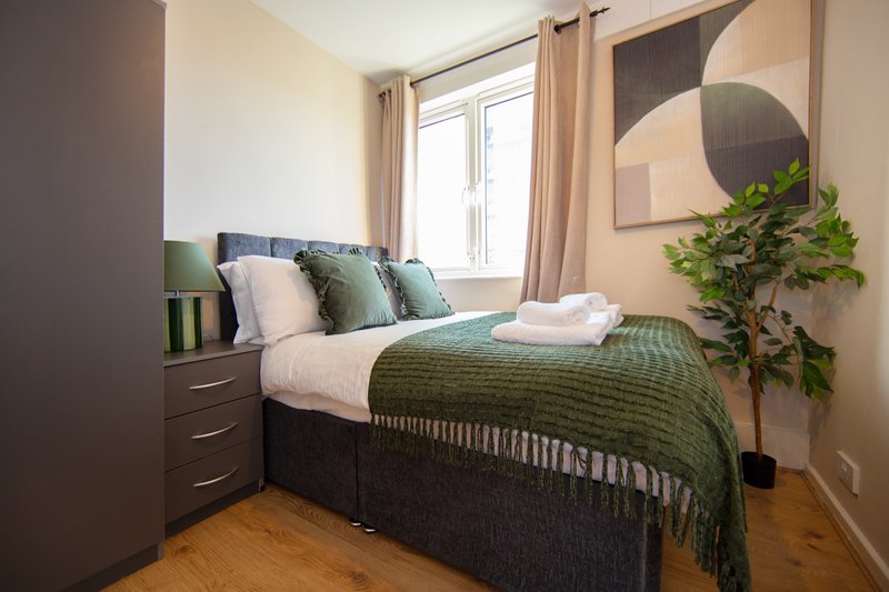 Compact bedroom with double bed, green bedding, wooden floor, and wall-mounted circular mirror