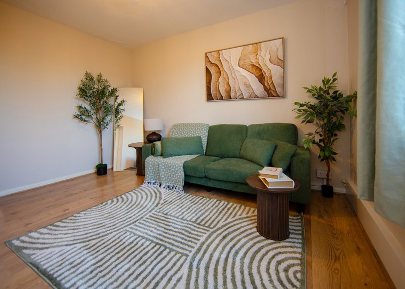 Living room with green sofa, striped rug, wooden floor, potted plants and wall art