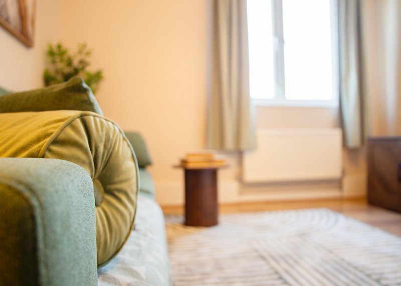 Bright living room with green sofa, yellow cushion, small table, potted plant, and window with curtains