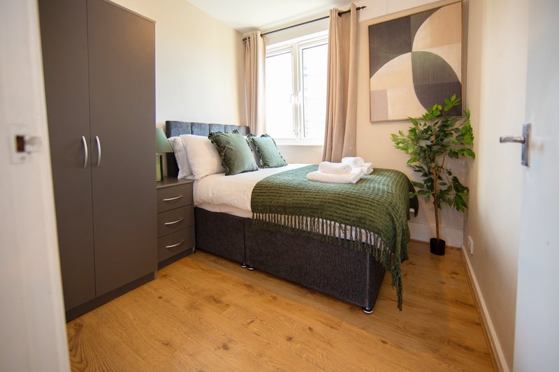 Compact bedroom with double bed, fitted wardrobe, circular mirror, potted plant and wooden floor