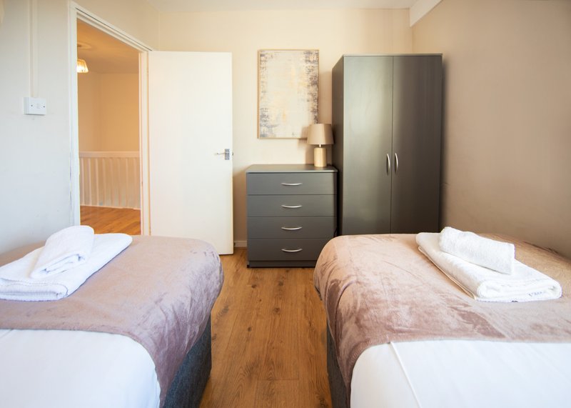Twin bedroom with wooden floor, two single beds, dark wardrobe and chest of drawers