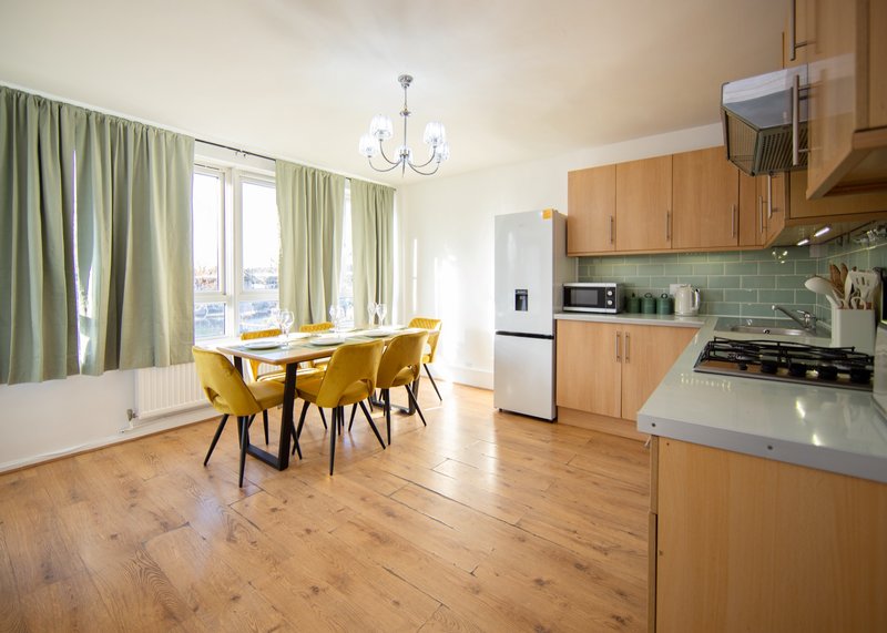 Open-plan kitchen and dining area with wooden flooring, yellow chairs, and sage green curtains
