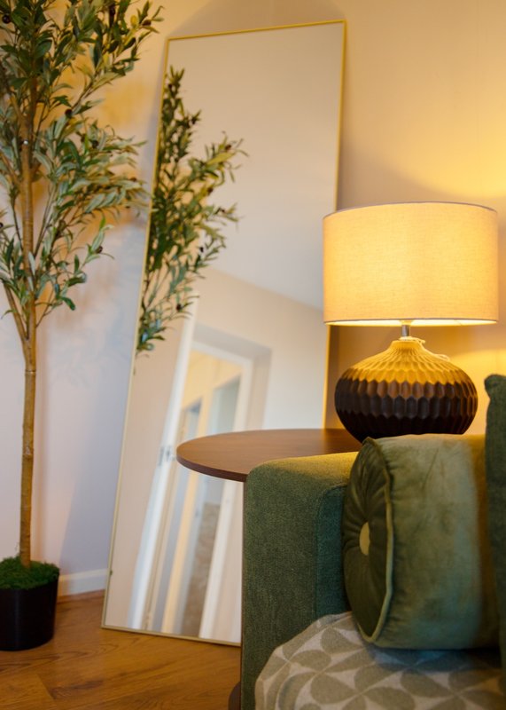 Modern bedroom corner with green upholstered chair, decorative lamp, mirror, and potted plant