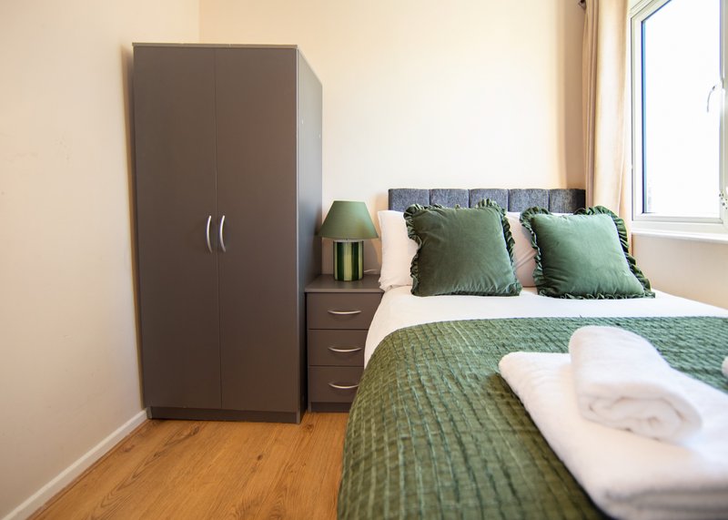 Modern bedroom with double bed, green bedding, dark wardrobe and wooden flooring