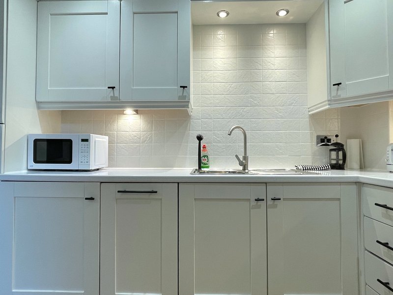 Modern kitchen with pale blue cabinetry, white subway tile backsplash, microwave and sink