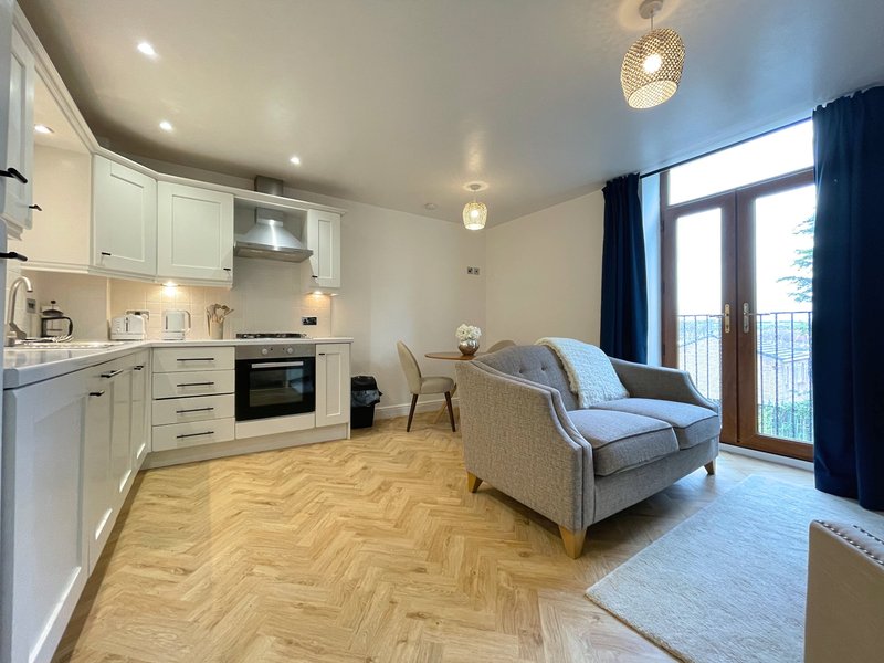 Open-plan kitchen and living area with white cabinetry, herringbone flooring, and blue armchair