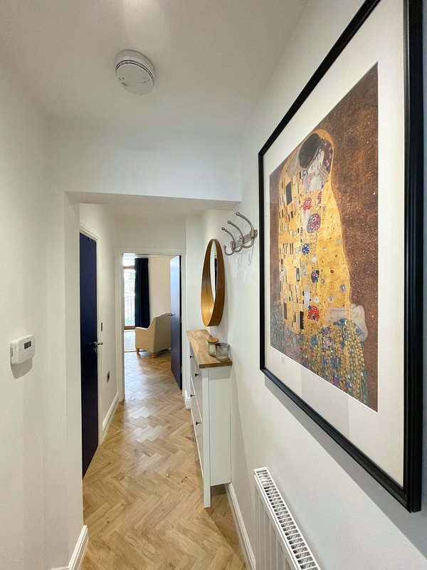 Bright hallway with herringbone wood flooring, framed art print, and doorways leading to other rooms