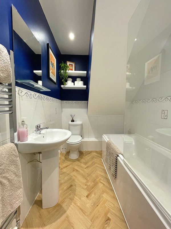 Modern bathroom with pedestal sink, toilet, bath, blue accent wall and shelving