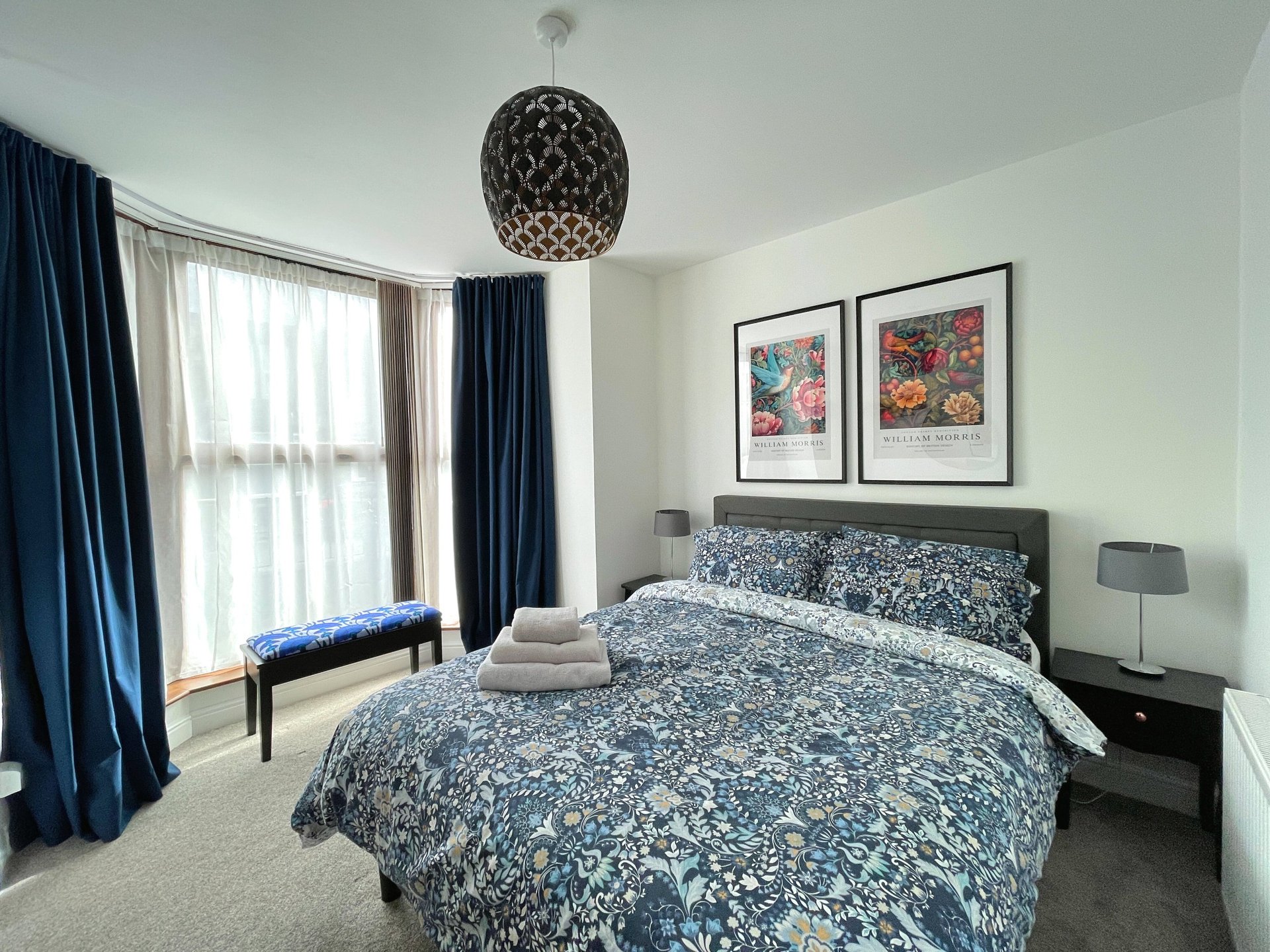 Modern bedroom with double bed, blue patterned bedding, pendant light, large window with curtains