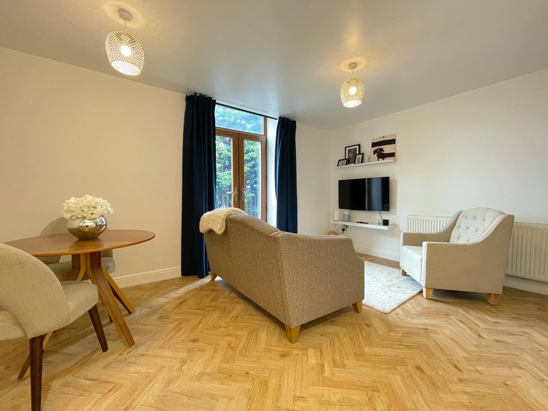 Bright living room with cream sofa, armchair, wooden side table, herringbone flooring and TV