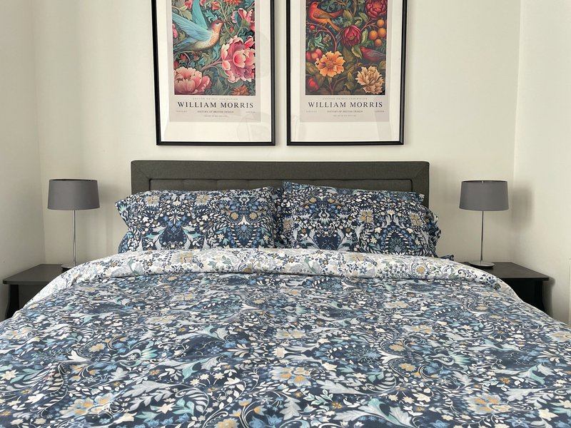 Bedroom with double bed, patterned blue bedding, dark headboard, two bedside lamps, and framed William Morris prints above bed
