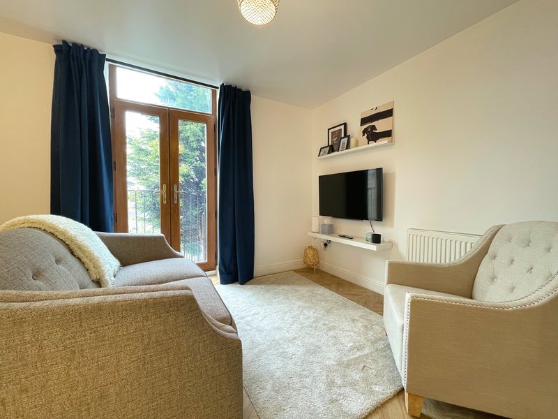 Bright living room with cream upholstered armchairs, TV on white unit, large windows with dark curtains