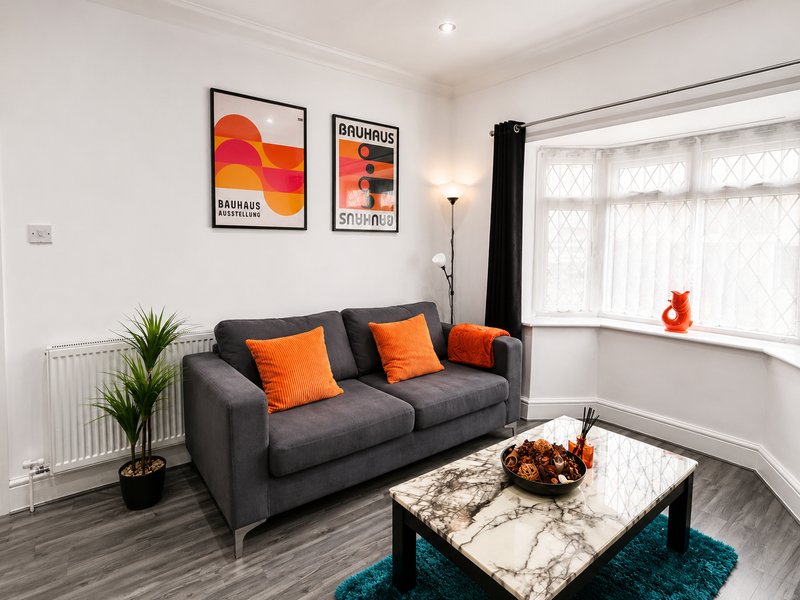 Modern living room with grey sofa, orange cushions, coffee table, and framed wall art