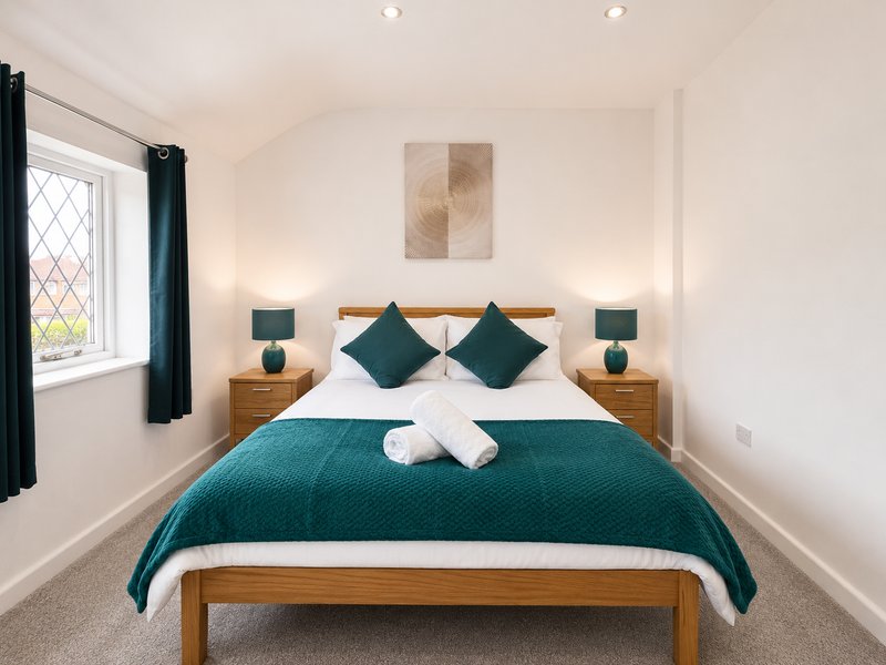 Bedroom with wooden bed frame, teal bedding, white pillows, and teal cushions
