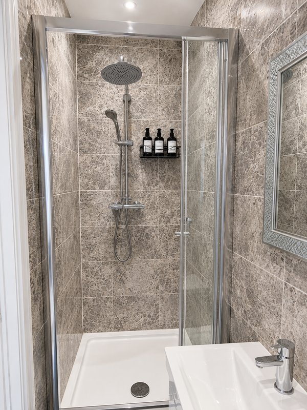 Modern bathroom shower enclosure with stone tile walls, rainfall showerhead and toiletries shelf