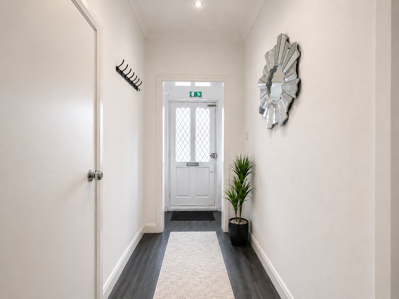 Bright hallway with white walls, dark wood flooring, potted plant and wall art