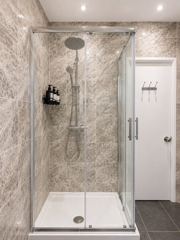 Modern shower enclosure with rainfall showerhead, glass doors, and marble-effect tiled walls