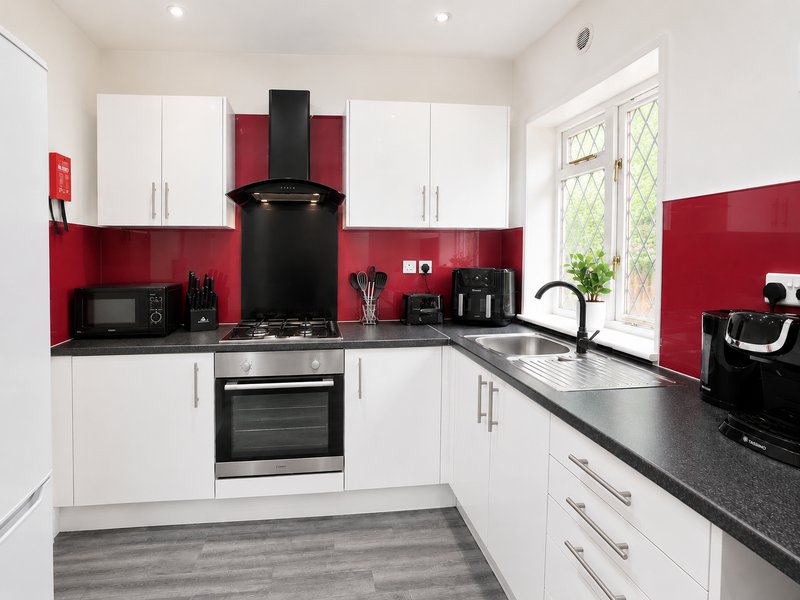 Modern kitchen with white cabinets, red backsplash, black countertops and stainless steel appliances