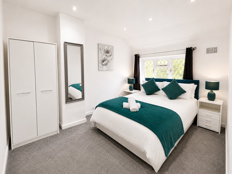 Modern bedroom with double bed, teal bedding, white wardrobe and bedside tables
