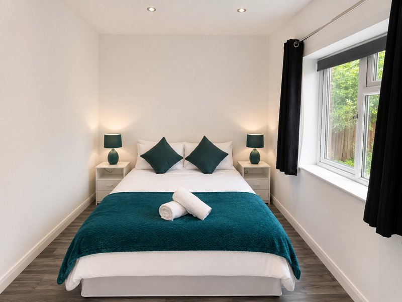 Modern bedroom with double bed, teal bedding, dark cushions, and bedside lamps