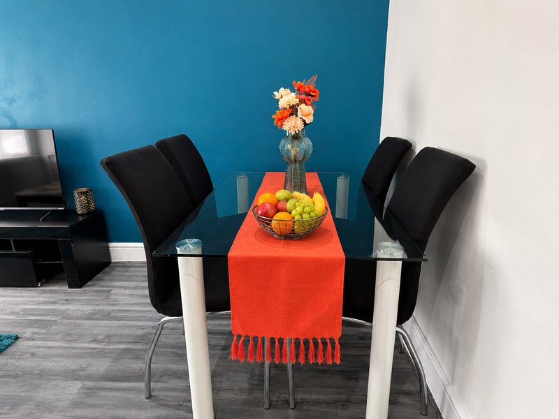 Dining area with blue accent wall, table with red runner, flowers in vase, and black chairs