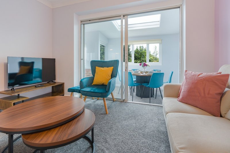 Modern living room with wooden coffee table, blue armchair, sofa with coral cushion, TV, and glass doors to garden