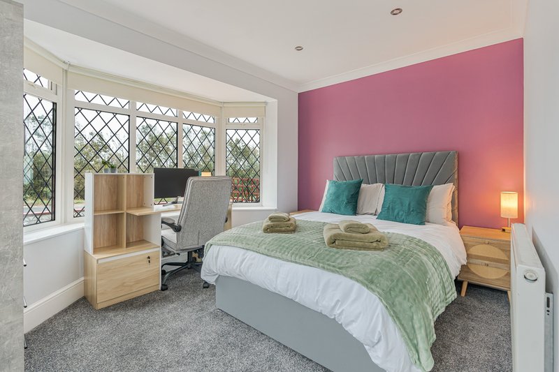 Bedroom with double bed, pink accent wall, window seat desk area, and wooden furnishings