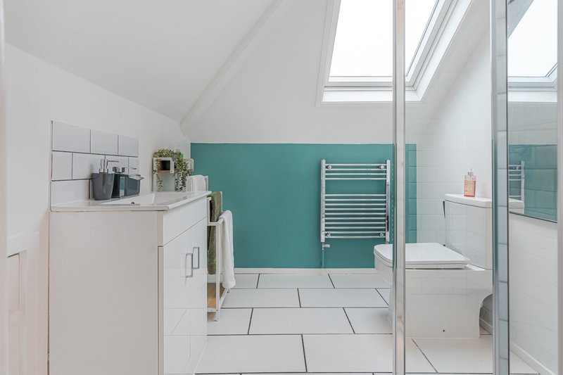 Modern bathroom with white vanity, turquoise accent wall, skylight and rainfall shower