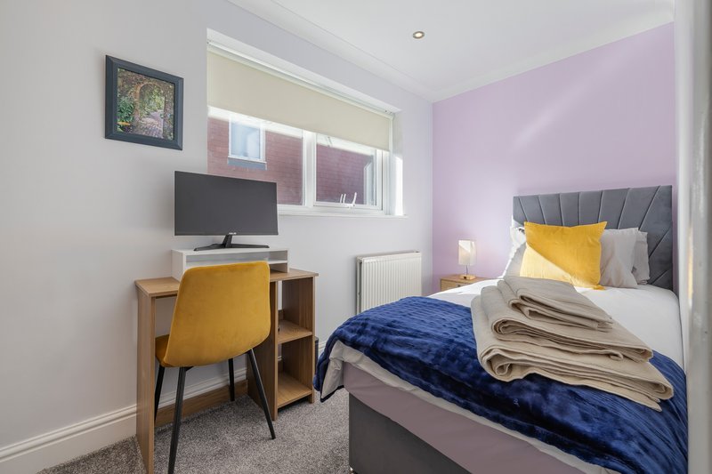 Bedroom with double bed, desk, chair, TV, and window with purple accent wall