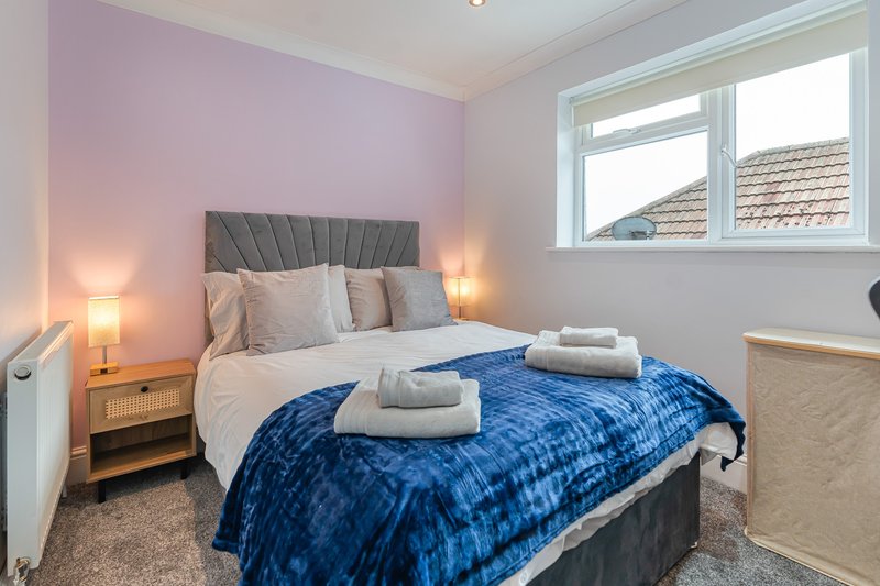Modern bedroom with double bed, blue quilted throw, grey headboard, and bedside lamps