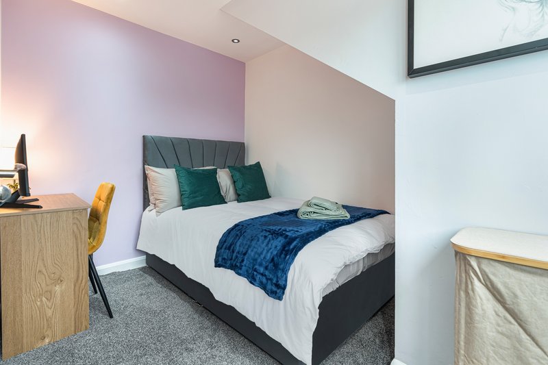 Modern bedroom with double bed, blue throw, green cushions, wooden desk and yellow chair