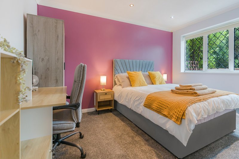 Modern bedroom with pink accent wall, double bed with yellow bedding, desk chair and window