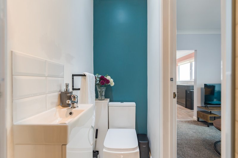 Compact bathroom with white sink, toilet, teal accent wall and fresh flowers in vase