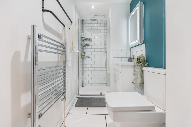 Modern bathroom with white subway tiles, towel rail, toilet, basin and teal accent wall
