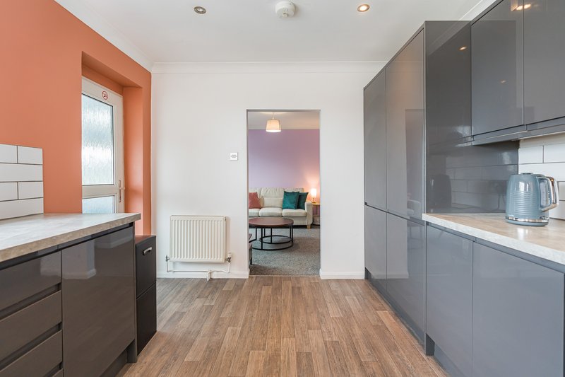 Modern kitchen with gray cabinetry, wood flooring, orange accent wall, and open-plan living space