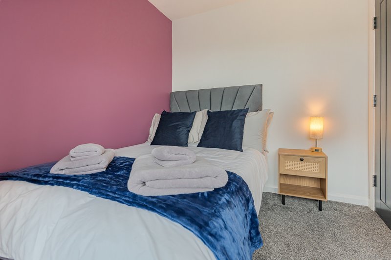Modern bedroom with pink accent wall, double bed, white pillows and blue bedding, wooden nightstand with lamp