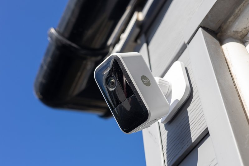 External security camera mounted on white building corner against blue sky