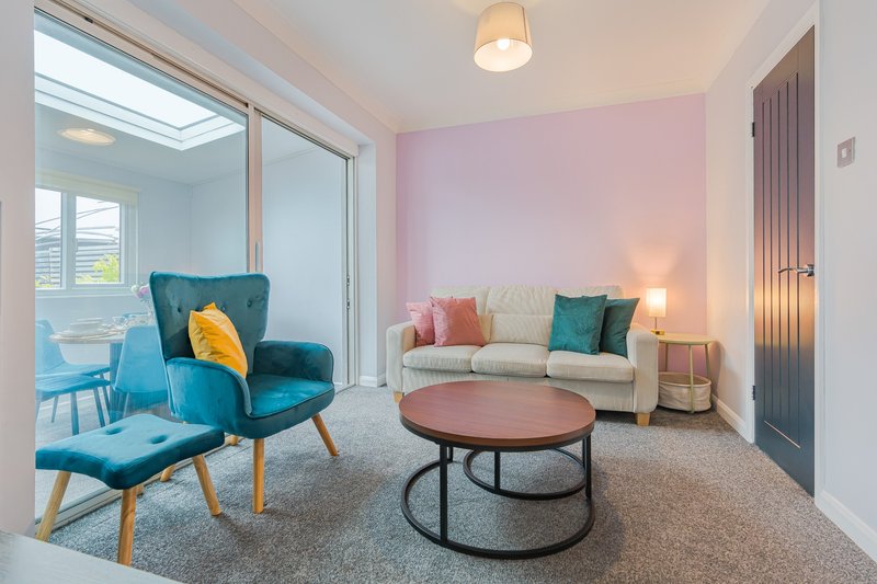 Modern living room with teal armchair, cream sofa, round coffee table and pink accent wall