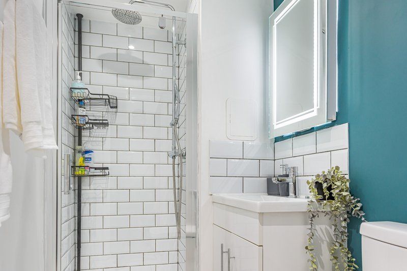 Modern bathroom with white subway tile shower, teal accent wall, vanity sink and illuminated mirror
