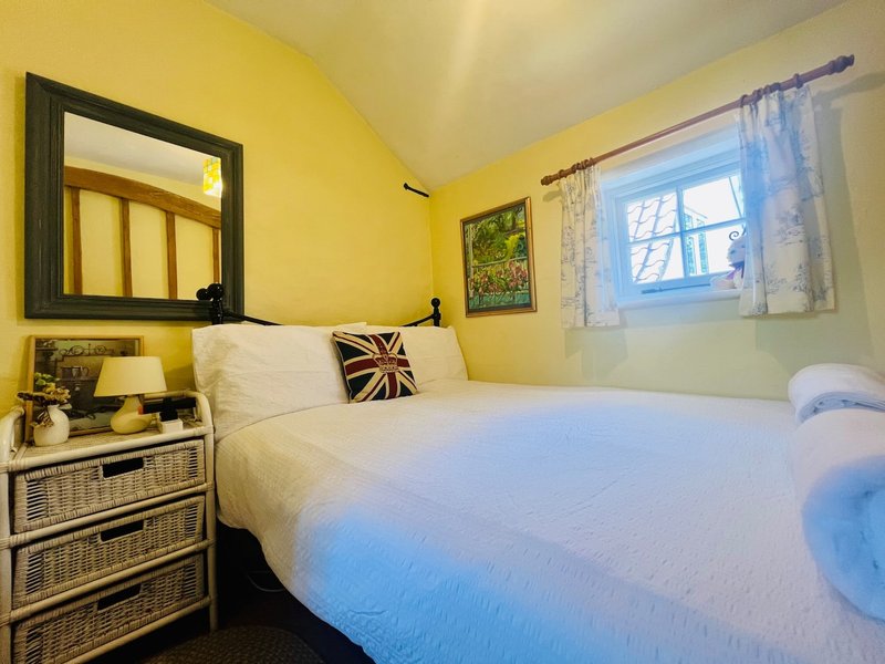 Bright yellow bedroom with double bed, wicker drawers, mirror and window with blue curtains