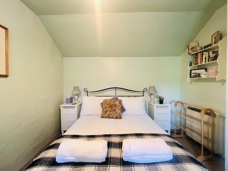 Bedroom with metal-frame bed, white bedding, decorative pillow, bedside tables, and wall shelves