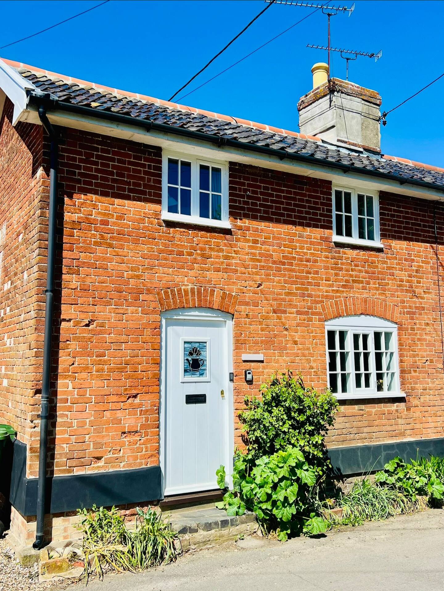 Red brick cottage exterior with white door, blue windows and chimney under clear sky