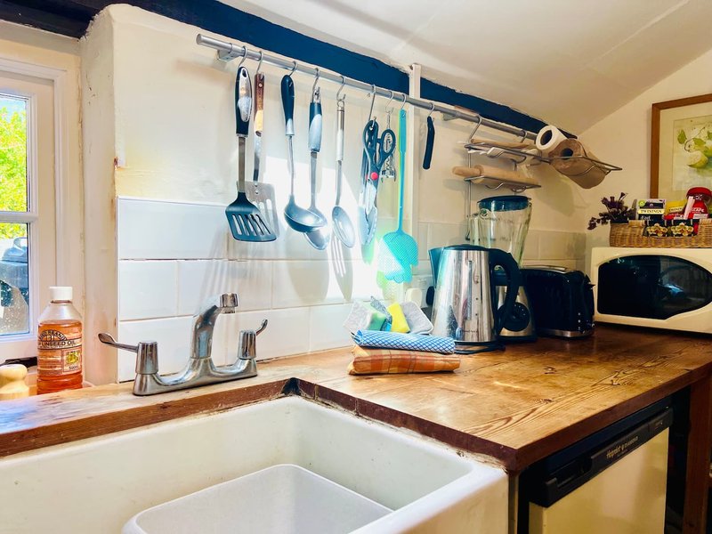 Kitchen with white sink, wooden countertop, utensils hanging on rail above window